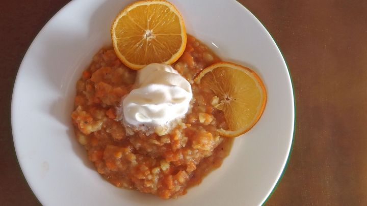 Eine cremige M&ouml;hren-Orangensuppe wird in einer Sch&uuml;ssel serviert, garniert mit Sahne und Orangenscheiben.