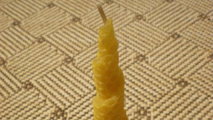 Eine gelbe, spiralf&ouml;rmige Kerze steht auf einem braunen Tonteller in einem gem&uuml;tlichen Raum mit einem gemusterten Teppich.