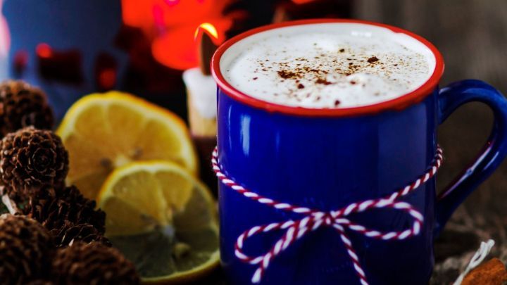 Eine blaue Tasse mit duftendem Punsch steht auf einem rustikalen Tisch, umgeben von Zimtstangen und Zitrone.