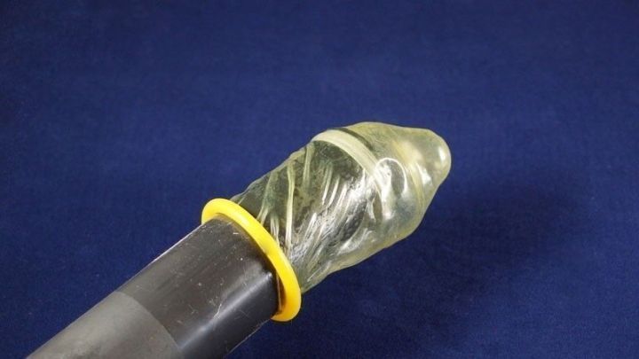 Ein Kondom sitzt an einem Staubsaugerrohr, um Spinnen beim Einsaugen sicher zu halten. Der Hintergrund ist einellblau.