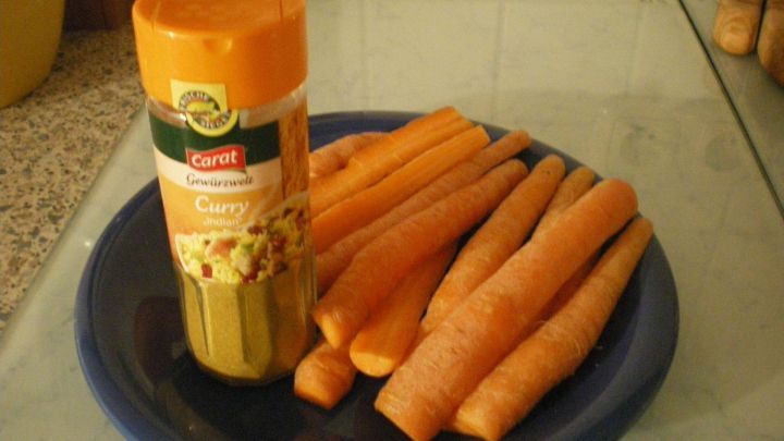 Karotten liegen auf einem blauen Teller neben einer Curry-Gew&uuml;rzdose in einer K&uuml;che. Text auf der Dose: "Carat Gew&uuml;rzwelt Curry indian".