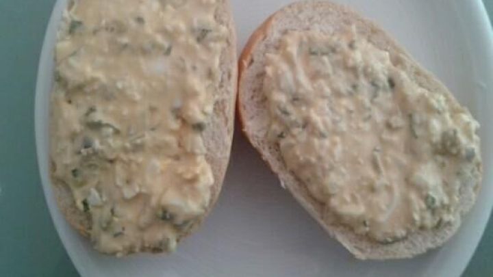 Die zwei Brotscheiben sind mit einem gelben Brotaufstrich aus Eiern und Kr&auml;utern bestrichen und liegen auf einem wei&szlig;en Teller.