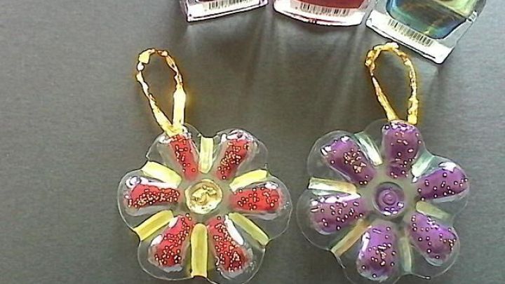 Zwei Deko Aufh&auml;nger aus PET-Flaschen in Bl&uuml;tenform h&auml;ngen mit goldenen Schleifen; Nagellackfarben im Hintergrund erg&auml;nzen die Farben.