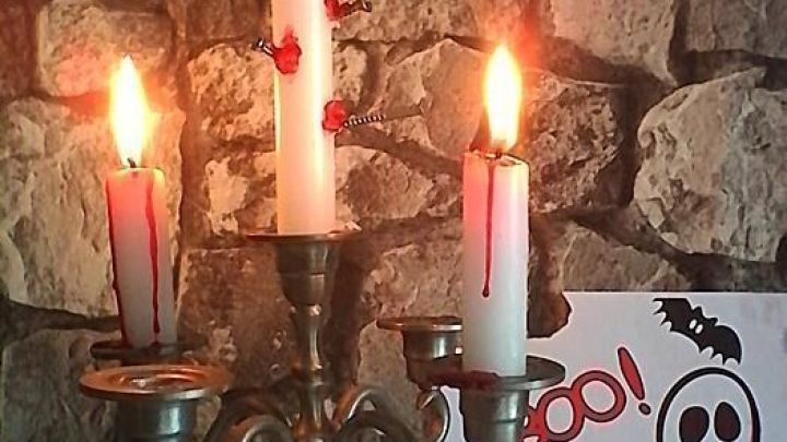 Ein Kandelaber mit blutenden Kerzen tropft Wachs, im Hintergrund eine Steinwand und ein Halloween-Bild mit K&uuml;rbis und Geist.