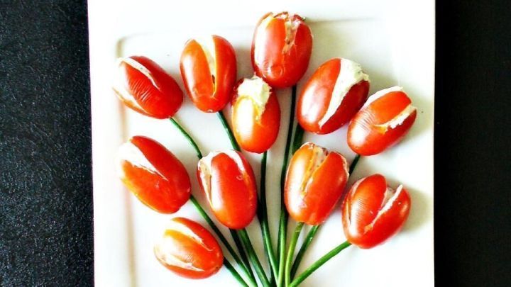 Ein Strau&szlig; aus pr&auml;parierten Tomaten sieht aus wie frische Tulpen, arrangiert auf einem wei&szlig;en Teller vor schwarzem Hintergrund.