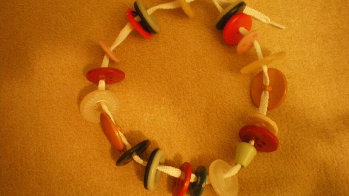 Eine bunte Knopfkette liegt kreisf&ouml;rmig auf einem beigen Hintergrund, aufgereiht auf einer wei&szlig;en Schnur.