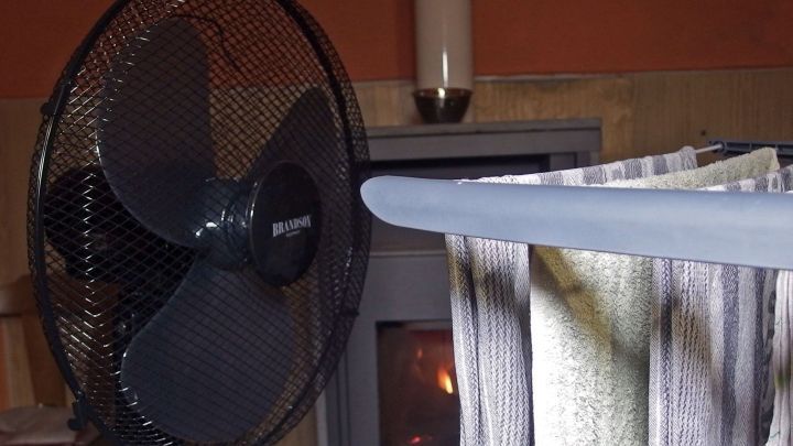 Ein W&auml;schest&auml;nder mit feuchter W&auml;sche steht neben einem Ventilator, der eine warme, kleine Wohnumgebung unterst&uuml;tzt.