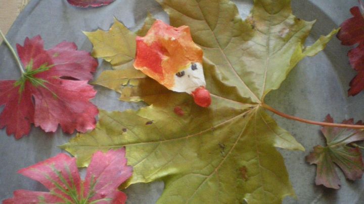 Ein kleiner Salzteig-Igel liegt auf einem gro&szlig;en, gr&uuml;nen Ahornblatt, umgeben von roten Herbstbl&auml;ttern auf einem Metalltablett.