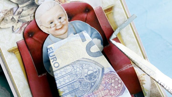 Eine kreative Gl&uuml;ckwunschkarte zeigt eine Figur im Sessel, die mit Geldscheinen dekoriert ist.