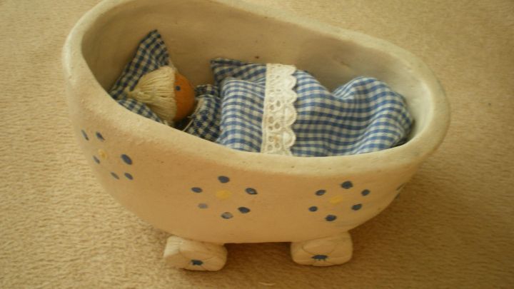 Ein kleiner Puppenwagen mit blauen Blumenmustern enth&auml;lt eine Puppe und ein kariertes Kissen, steht auf Teppichboden.