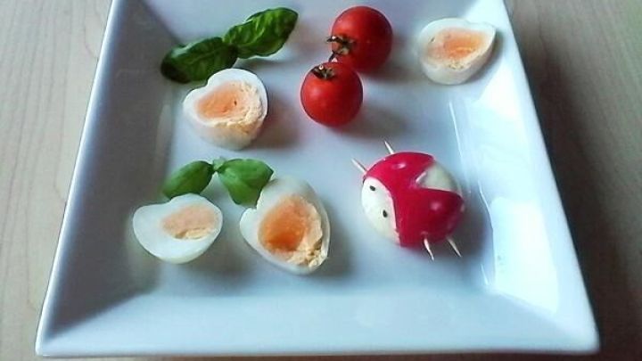 Herzh&uuml;lsen gef&uuml;llte Eier liegen auf einem Teller, umgeben von Tomaten und Basilikum, dekorativ angerichtet.