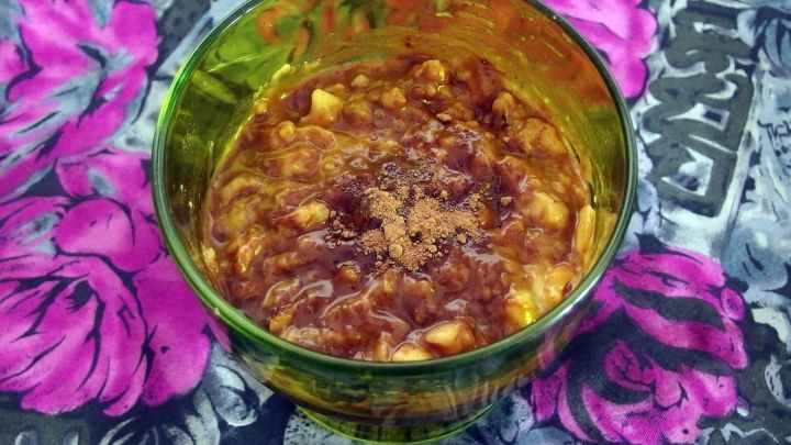 Ein bunter Becher mit einer schokoladigen Bananenmischung steht auf einem blumigen Hintergrund.