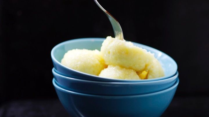 Runde Kl&ouml;&szlig;e werden mit einer Gabel aus einer blauen Sch&uuml;ssel gehoben, vor einem dunklen Hintergrund.