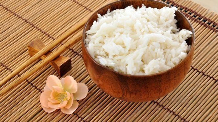 Eine Schale mit gekochtem Reis steht auf einer Bambusmatte neben Essst&auml;bchen und einer dekorativen Bl&uuml;te.