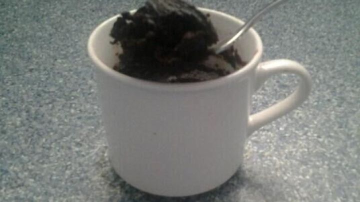 Ein wei&szlig;er Becher mit einem schokoladigen, veganen Mikrowellen-Brownie steht auf einer blauen Arbeitsplatte.