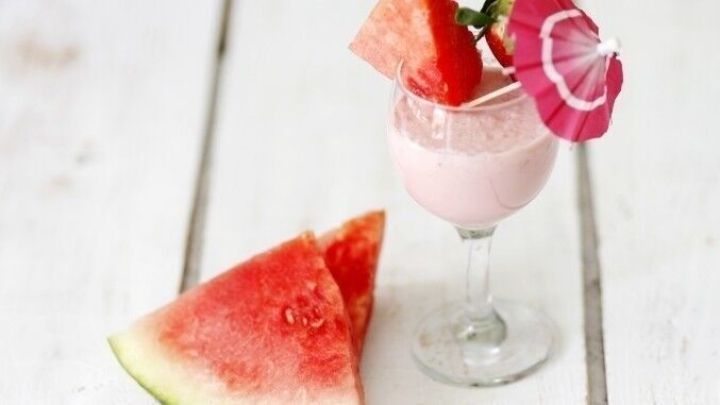 Ein erfrischender Melonen-Joghurt-Drink in einem Glas, dekoriert mit Melonenscheiben und einer Blume, auf einem rustikalen Tisch.