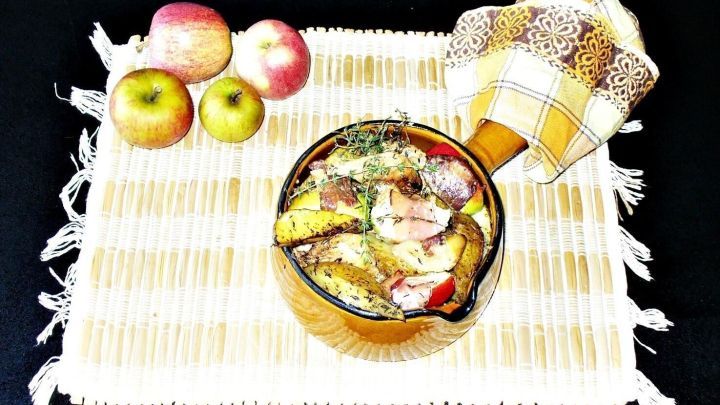 In einer Sch&uuml;ssel sind Speck&auml;pfel mit H&auml;hnchenbrust und Thymiankartoffeln angerichtet, umgeben von frischen &Auml;pfeln auf einem Tisch.