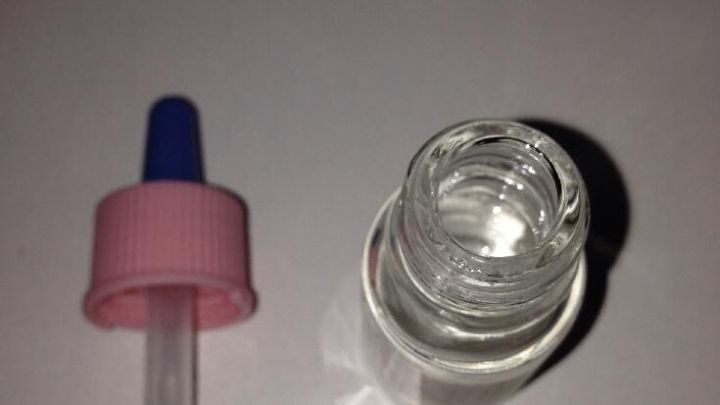 Eine Glasflasche mit Duft&ouml;l steht auf einem wei&szlig;en Tisch, daneben liegt eine Pipette zum genauen Dosieren.