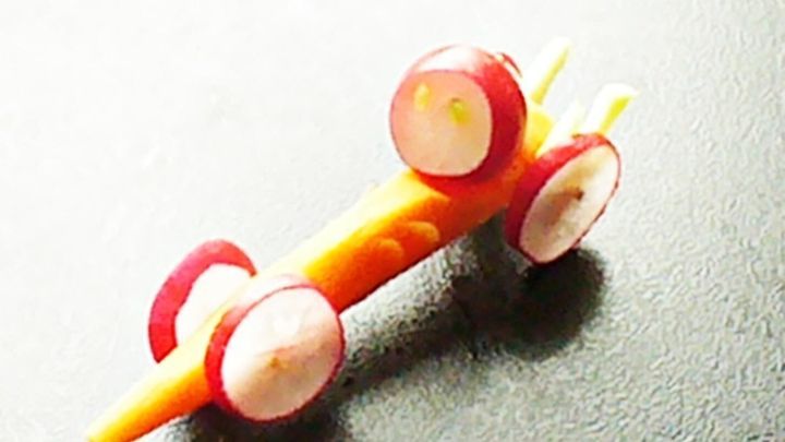 Ein Wagen aus Karotte und Radieschen steht auf einer dunklen Oberfl&auml;che, bereit f&uuml;r ein kreatives Rennen mit Gem&uuml;se.