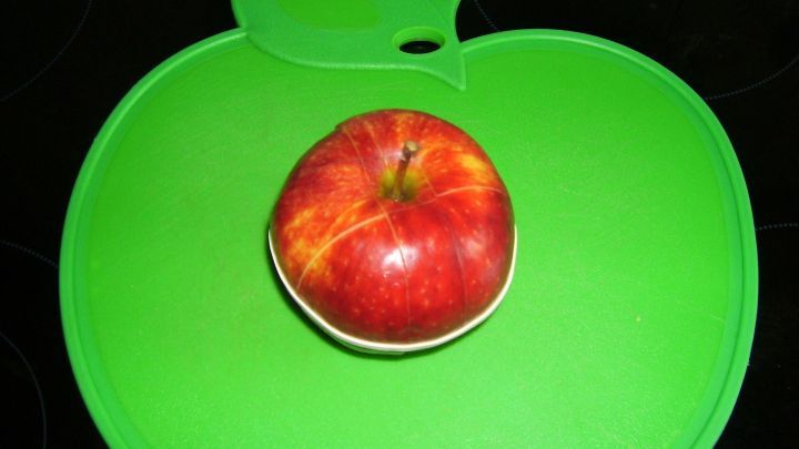 Ein roter, geschnittener Apfel liegt auf einem gr&uuml;nen, apfelf&ouml;rmigen Schneidebrett in einer modernen K&uuml;che.