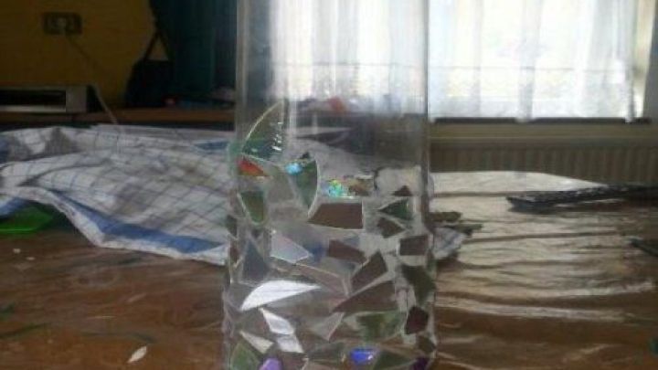 Eine alte Vase mit bunten Mosaikst&uuml;cken steht auf einem Tisch in einem hellen Raum und reflektiert das Licht.