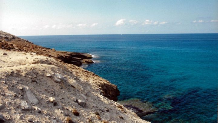 Blauer Ozean bietet Salzwasser, das sanft die felsige K&uuml;ste umsp&uuml;lt, bei strahlendem Himmel und ruhiger Atmosph&auml;re.