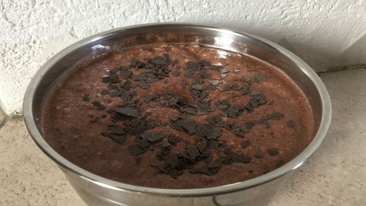 Ein Pumpernickel-Parfait in einer metallenen Sch&uuml;ssel, cremig und mit Kakaost&uuml;ckchen dekoriert, steht auf einer hellen Oberfl&auml;che.