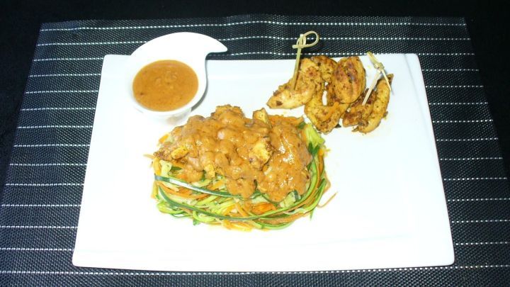 Zucchini-Karotten-Spaghetti sind auf einem wei&szlig;en Teller angerichtet, garniert mit Erdnussso&szlig;e und zarter Pute.