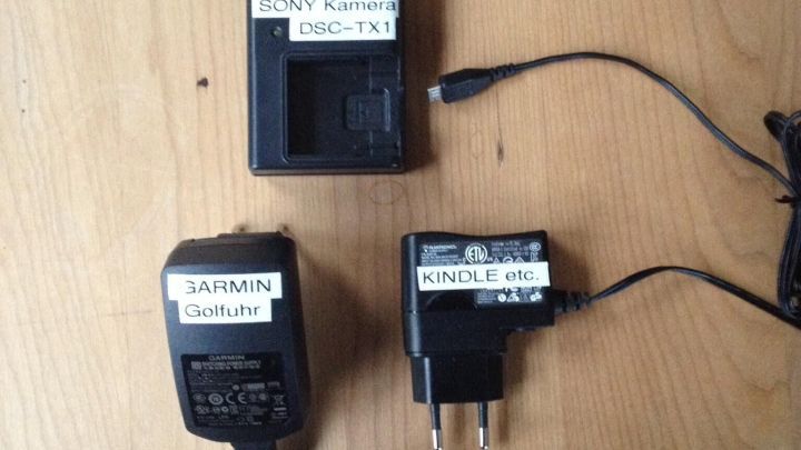 Drei Netzteile liegen auf einem Holztisch, beschriftet zur Identifikation, um Verwechslungen zu vermeiden.