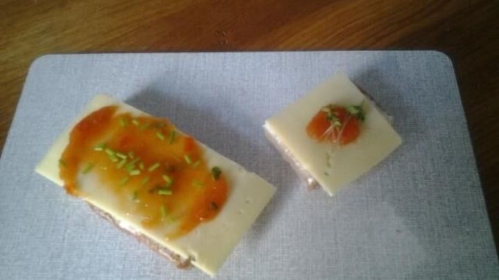 Zwei belegte Brotscheiben mit K&auml;sescheiben und feurig-s&uuml;&szlig;em Paprikamus, dekoriert mit Schnittlauch, auf Schneidebrett.