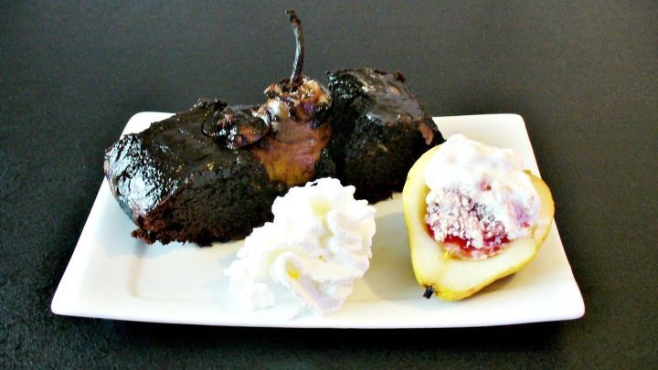 Ein k&ouml;stlicher Schokoladenkuchen mit ganzen Birnen und Sahne auf einem wei&szlig;en Teller vor einem dunklen Hintergrund.