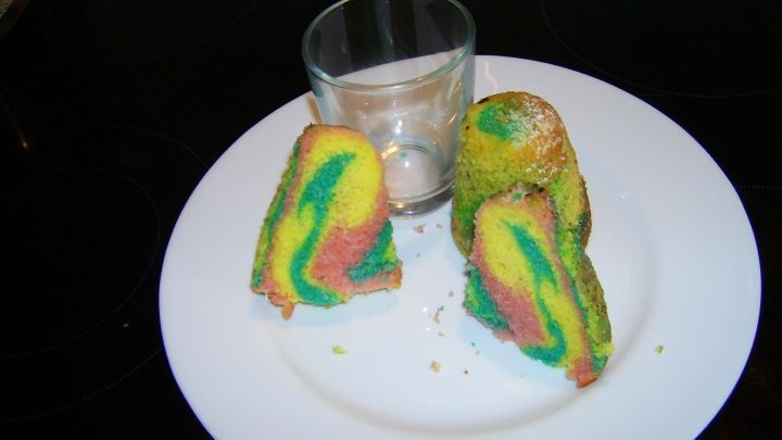 Bunte, marmorierte Kuchenst&uuml;cke liegen auf einem wei&szlig;en Teller, w&auml;hrend ein leeres Glas f&uuml;r Duftkerzen daneben steht.