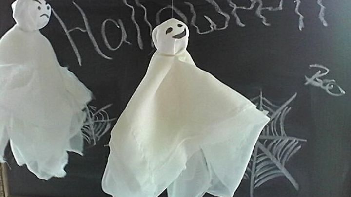 Zwei fliegende Halloween-Gespenster h&auml;ngen &uuml;ber einer Tafel, auf der "Halloween" geschrieben steht, umgeben von Spinnennetzen.