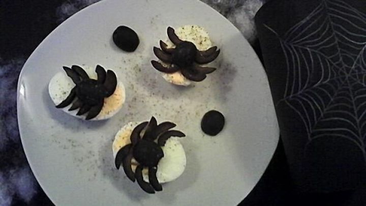 Gruslige Spinneneier auf einem Teller, dekoriert mit essbaren Spinnen, liegen im d&uuml;steren Halloween-Kontext.