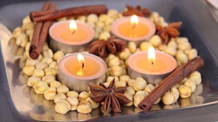 Teelichter brennen auf einem Teller, umgeben von Zimtstangen, Sternanis und Haseln&uuml;ssen in einem gem&uuml;tlichen Arrangement.