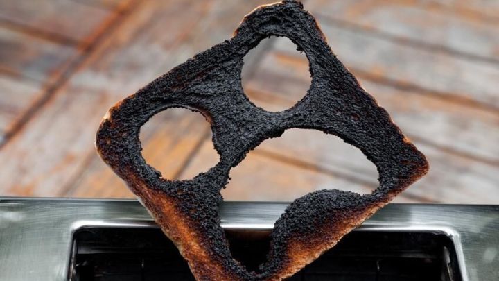 Ein verbranntes Toastbrot steckt in einem Toaster, umgeben von Holzboden; Acrylamid entsteht beim starken R&ouml;sten.