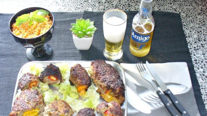 Gef&uuml;llte Paprikaschoten im Hackfleischmantel liegen auf einer Platte, umgeben von Salat, Bier und Reis.