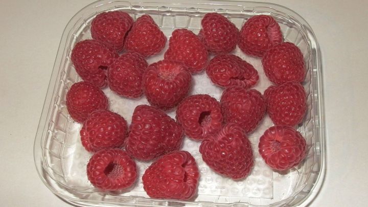 Eine Schale mit frischen, roten Himbeeren liegt auf einer wei&szlig;en Tischoberfl&auml;che und wartet darauf, beim Einkaufen von Lebensmitteln ausgew&auml;hlt zu werden.