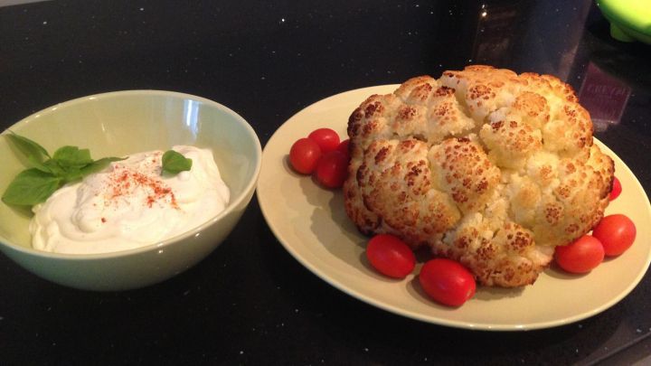 Ger&ouml;steter Blumenkohl steht auf einem Teller, umgeben von Cherry-Tomaten, neben einer Schale mit Ziegenk&auml;secreme.