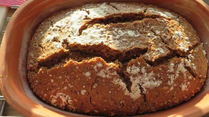 Ein frisch gebackenes Sauerteig Kraftbrot liegt in einer Tontopf-Form auf einem Tisch und wartet auf das Servieren.