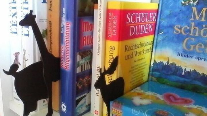 Schwarze Buchst&uuml;tzen in Form von Tieren stehen neben bunten B&uuml;cherreihen in einem hellen B&uuml;cherregal.