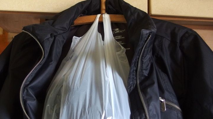 Eine Jacke h&auml;ngt an einem Kleiderhaken, w&auml;hrend eine durchsichtige T&uuml;te mit einem Schal, Handschuhen und einer M&uuml;tze darin befestigt ist.