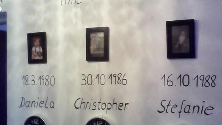 An der Wand sind drei Uhren und Bilder eingerahmt, die besondere Momente und Namen von Kindern hervorheben.