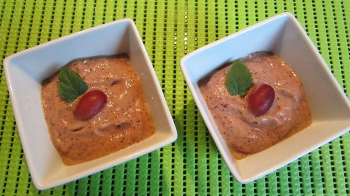 Zwei kleine Schalen mit cremiger Eiscreme, garniert mit einer Traube und Minze, stehen auf einer gr&uuml;nen Unterlage.