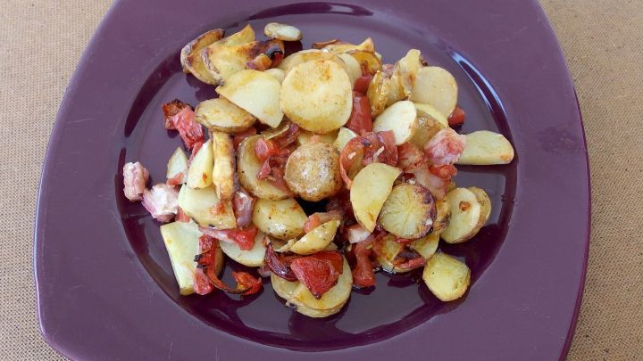 Gebackene Kartoffeln liegen appetitlich auf einem lila Teller, umgeben von knusprigem Speck und Zwiebeln.