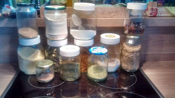 Eine Reihe von Schraubdeckelgl&auml;sern steht auf der Arbeitsfl&auml;che und enth&auml;lt verschiedene Zutaten wie Kr&auml;uter und Gew&uuml;rze.