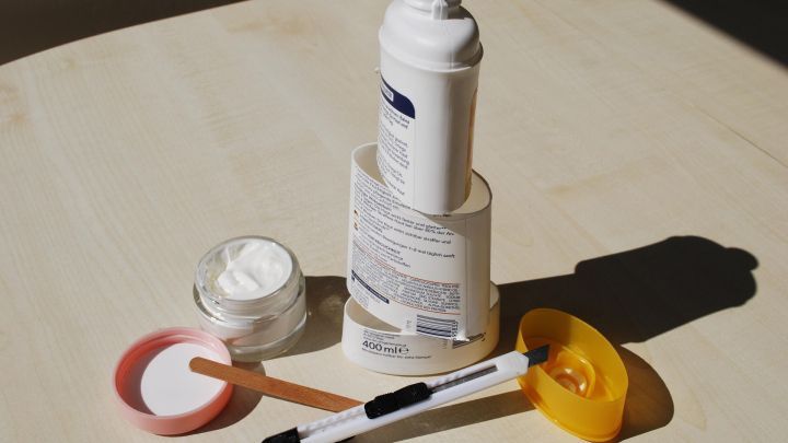 Eine K&ouml;rperlotion steht auf einem Tisch, w&auml;hrend ein Spatel und Beh&auml;lter sie f&uuml;r die Restnutzung vorbereiten.