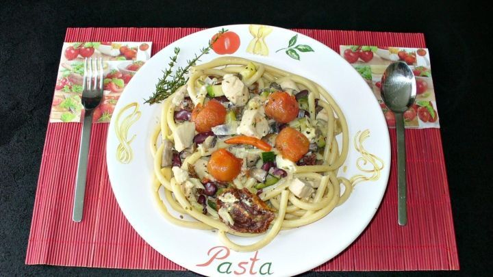 Ein Teller cremiger Spaghetti mit Gem&uuml;se und H&uuml;hnerfleisch liegt auf einem Tisch, umgeben von Besteck und einem dekorativen Platzset.