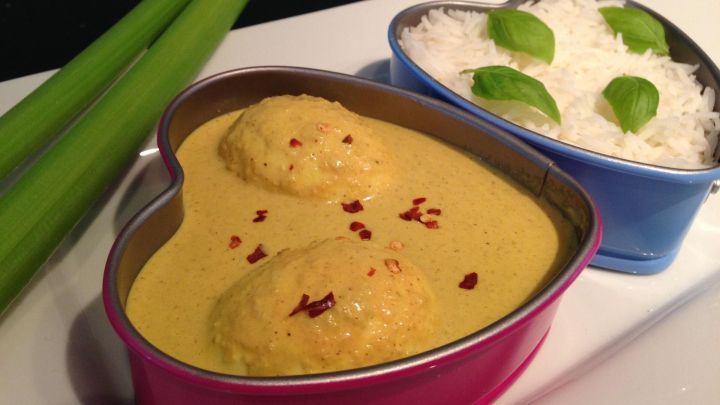 Ein herzf&ouml;rmiger Beh&auml;lter enth&auml;lt ein cremiges vegetarisches Eier-Curry, serviert mit Reis und frischen Kr&auml;utern.