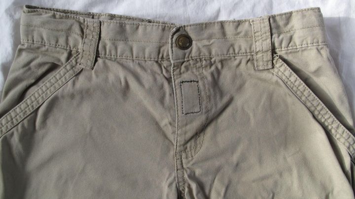 Beige Kinderhose mit defektem Rei&szlig;verschluss auf einem wei&szlig;en Untergrund, bereit zum Ersetzen durch Klettband.